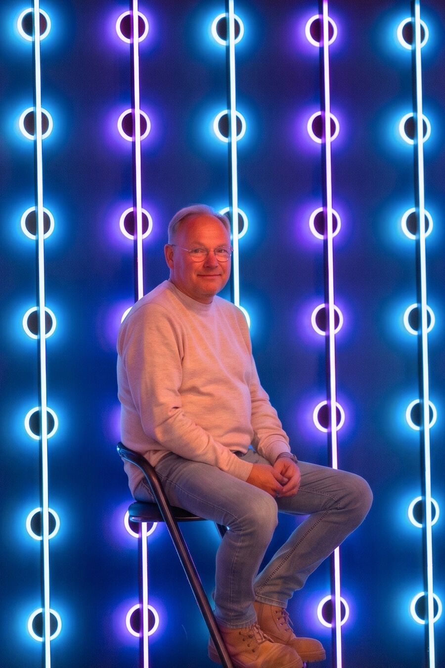 Jan Spies von Signs4U vor einer Leuchtwand aus blau und violett leuchtenden LED-Elementen.